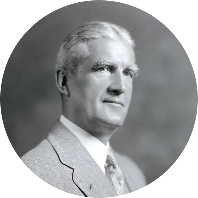 Black-and-white portrait of an older man in a suit and tie, shown in profile against a neutral background