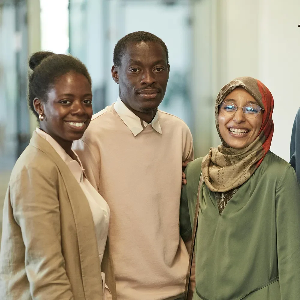 Three people standing together indoors, smiling at the camera.
