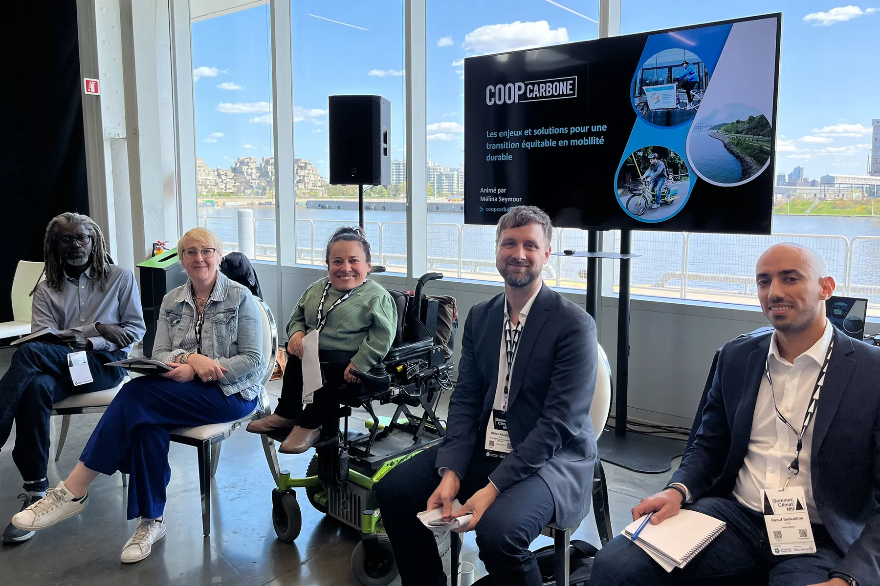 Panel discussion with seated speakers in a bright room overlooking water through large windows