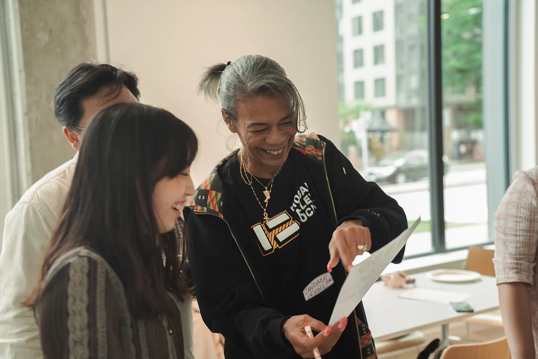 Person smiling while handing a document to another person indoors near a window.
